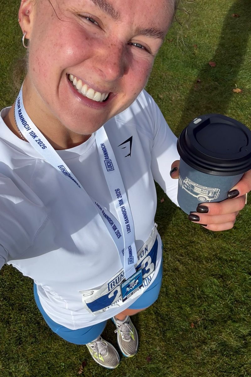 Sarah smiling with her 10K medal and a coffee